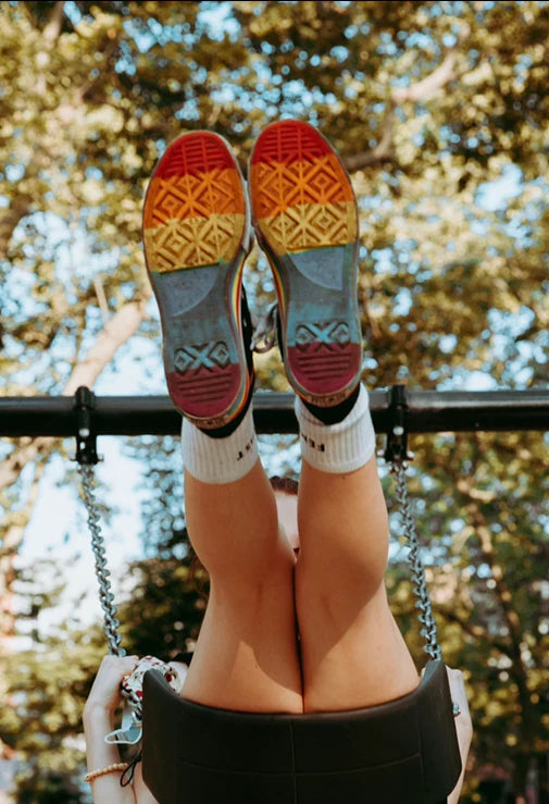 Rainbow sneakers kicked up in the air on a swing